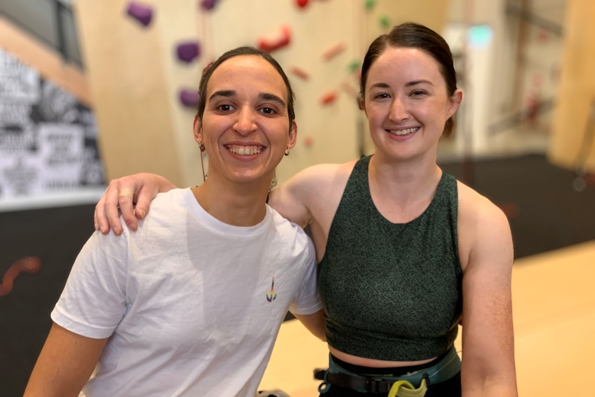Sarah Larcombe and Araminta McLennan smile as they stand beside one another in a rock climbing room.