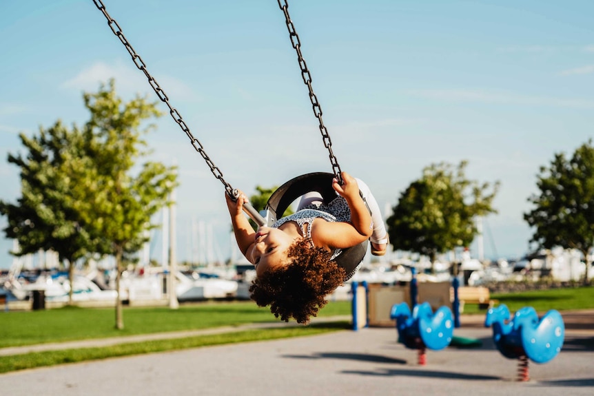 Young girl on a swing at the playground with her head looking back, for a story about child safety and helicopter parenting.