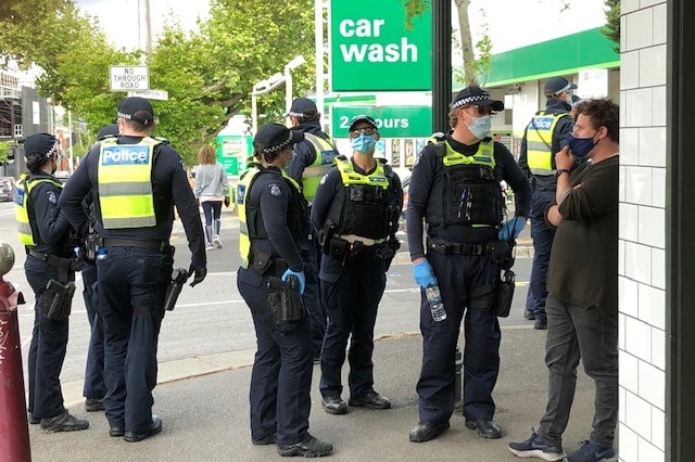 Eight armed police officers wearing blue surgical masks and plastic gloves on a street corner in Richmond.