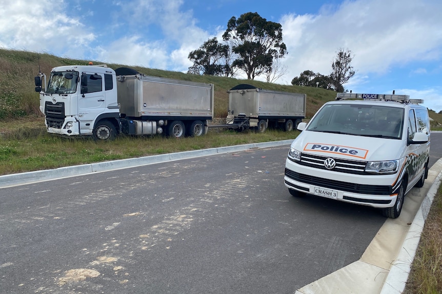A truck parked on the grass strip of a road and a police van near