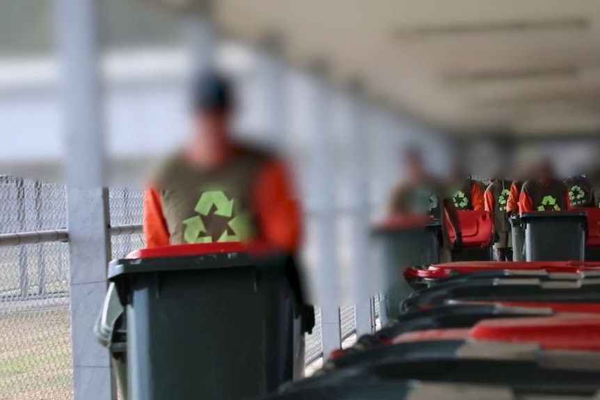 The face of a prisoner is blurred as he pushes a wheelie bin through a jail.