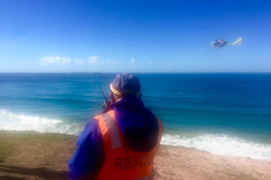A volunteer rescue worker with a walkie talkie and the Westpac Rescue helicopter on Red Rock headland.