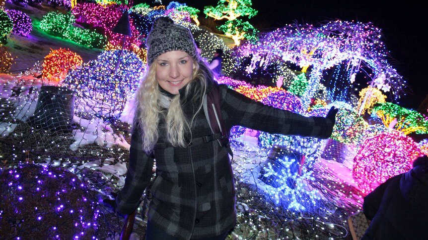 Marianka Heumann smiles for a photo standing in front of a light display at night.