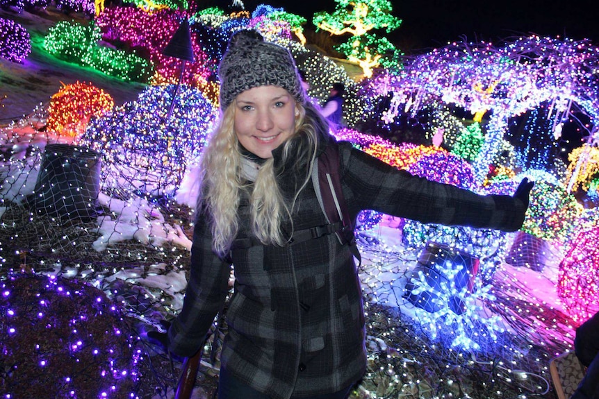 Marianka Heumann smiles for a photo standing in front of a light display at night.