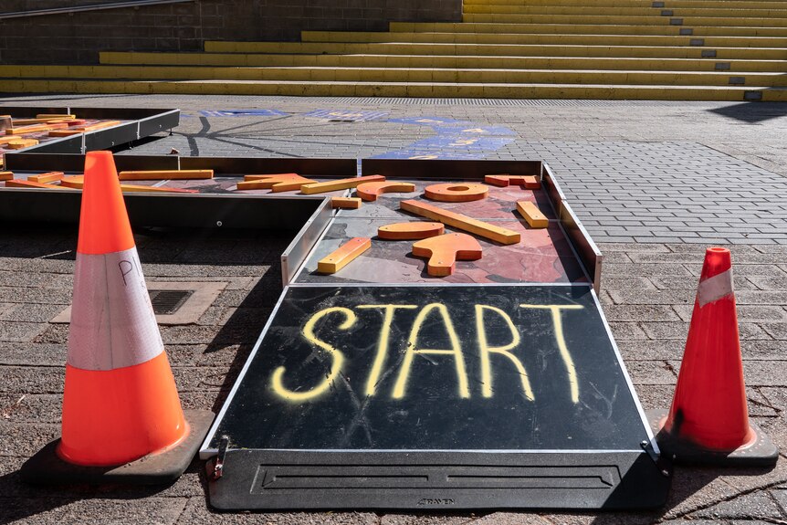 The start of of an obstacle course, with the word "start" written on a tile, with witch's hats on either side