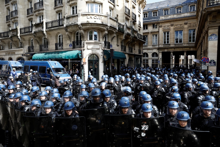 a huge crowd of police in riot gear stand guard in front of the constitutional court in paris