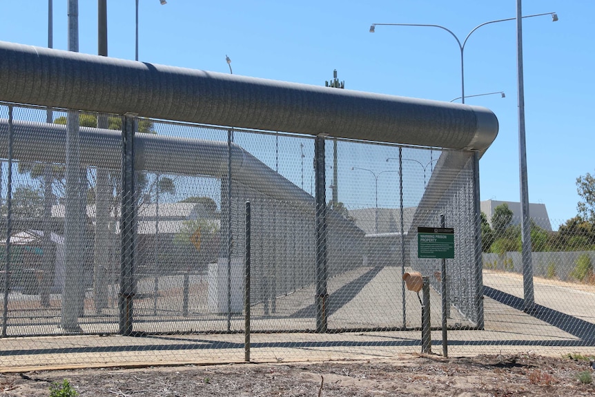 Wire fence outside Perth's Hakea Prison with prison building visible in background