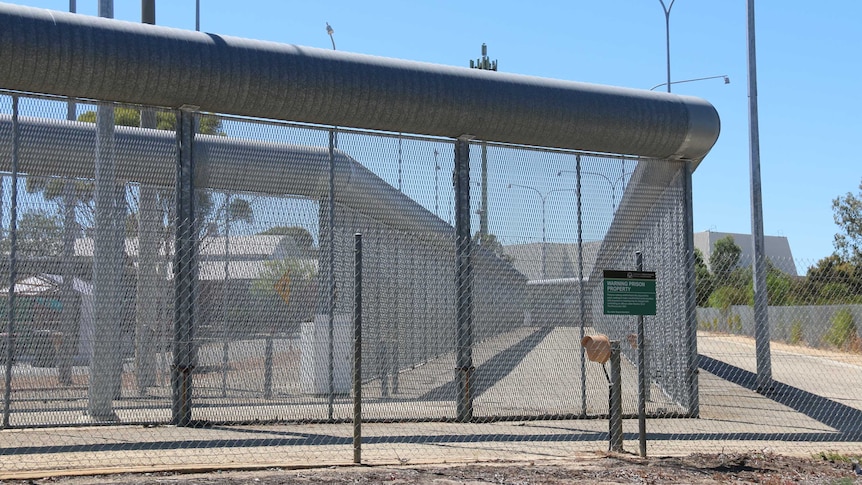 A wide shot of a large wire fence outside Perth's Hakea Prison with a prison building visible in the background.