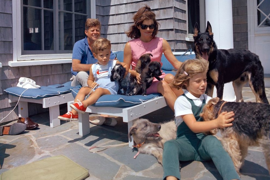 JFK and his family sit outside a house accompanied by six dogs.