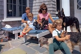 JFK and his family sit outside a house accompanied by six dogs.