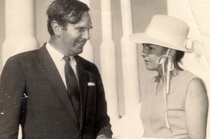 Old black and white photo of Ian Sinclair in a suit providing an envelope to Peggy Westmoreland in a dress and hat.