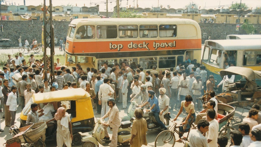 a large bus parked in a bustling delhi street