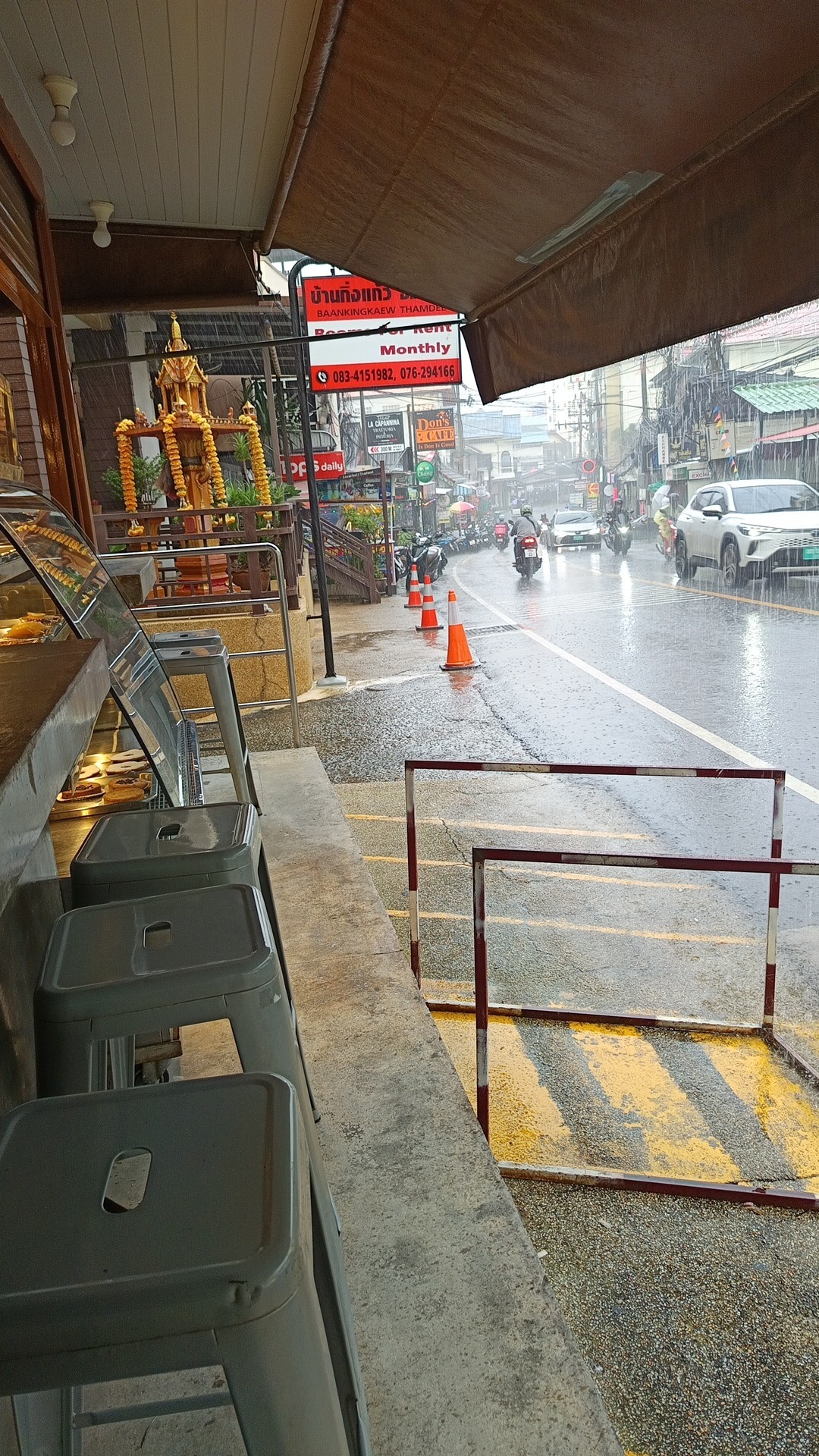 Rain pouring down on a street in Thailand with cars and motorbikes on the road.
