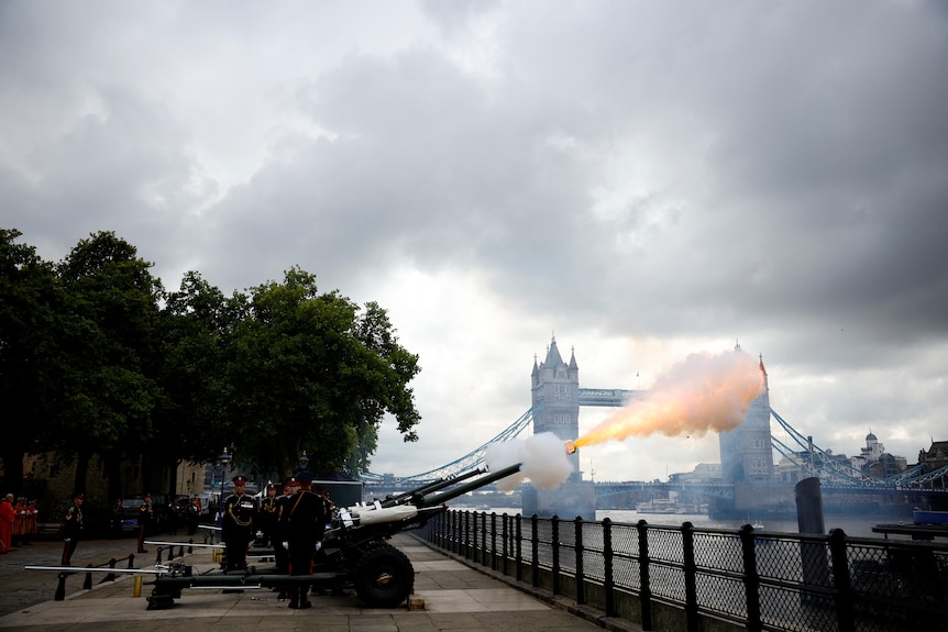A gun salute is fired with the London Bridge in the background. 
