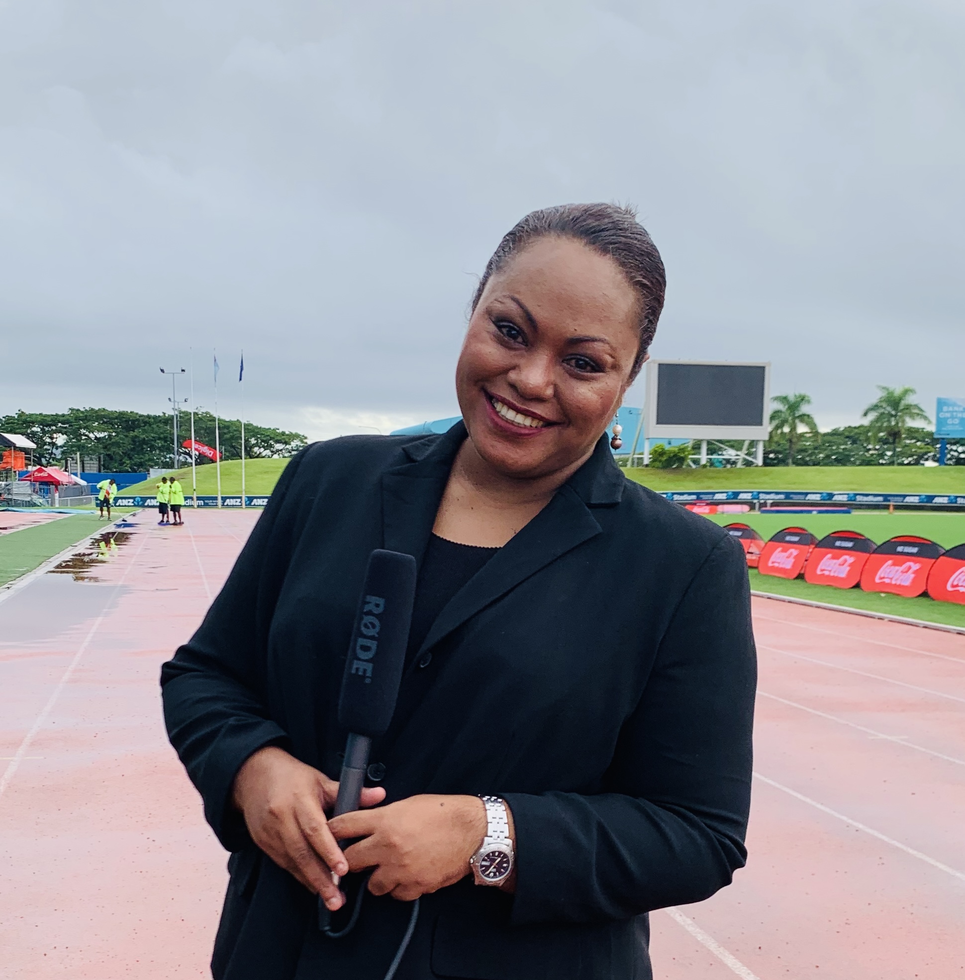 A woman holding a microphone standing on a sports running track on a gloomy day