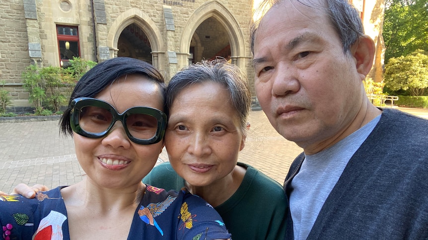 Grace Feng Fang Juan smiles as she poses for a selfie with her parents in front of an old stone building