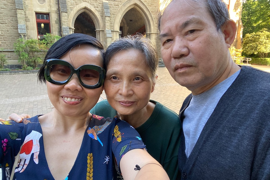 Grace Feng Fang Juan smiles as she poses for a selfie with her parents in front of an old stone building