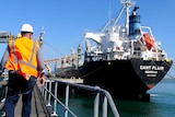 A man in a high-visibility vest and hard helmet walking up a ramp towards a cargo ship.