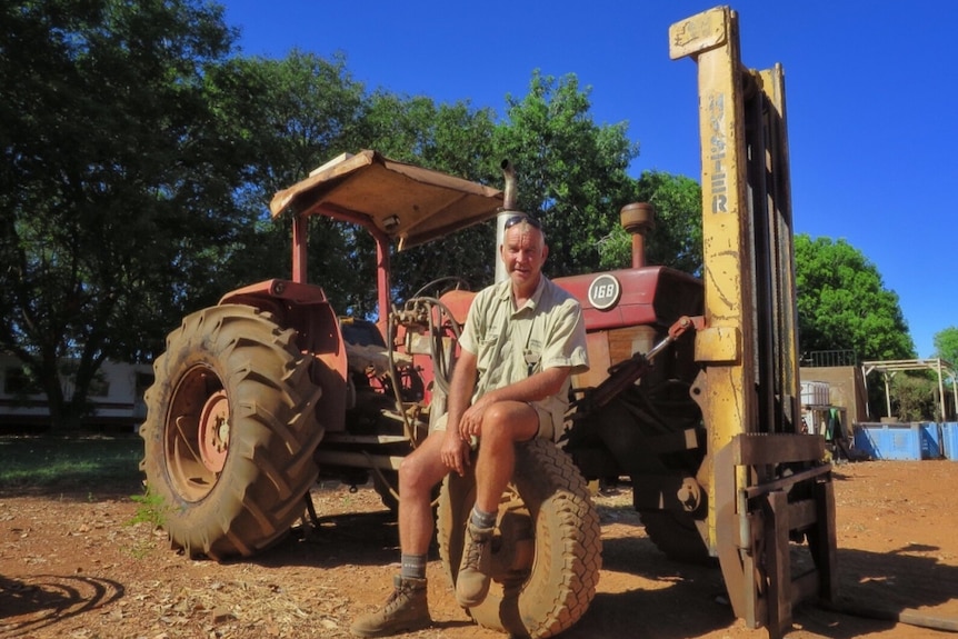 Farmer Lachlan Dobson sits on the wheel of a vintage tractor