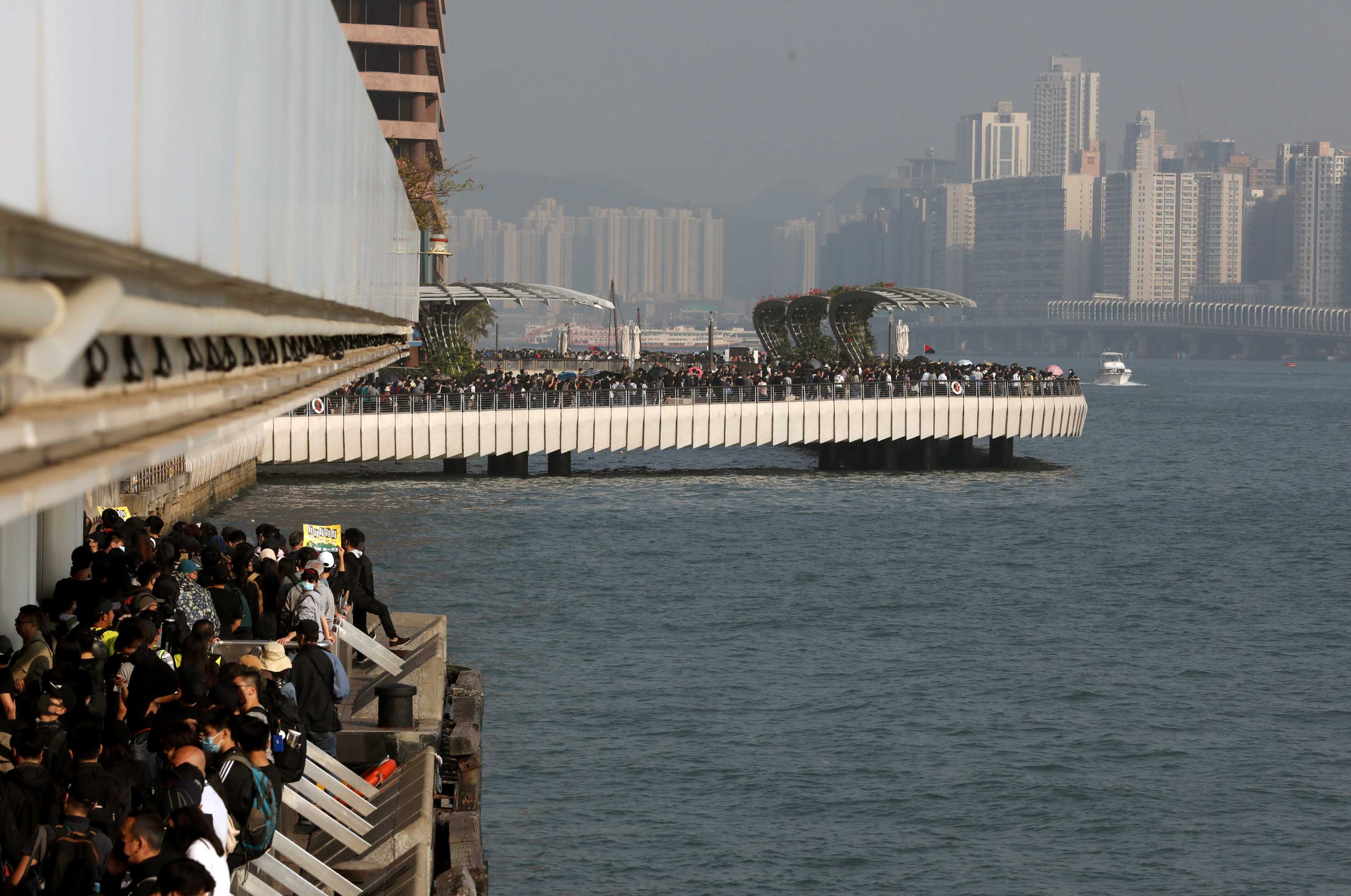 Looking below to jetties on Hong Kong's waterfront, you view large crowds of protesters filling all available space.