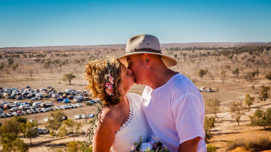 A couple kiss during a wedding ceremony with desert and cars in the background