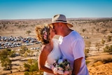 A couple kiss during a wedding ceremony with desert and cars in the background