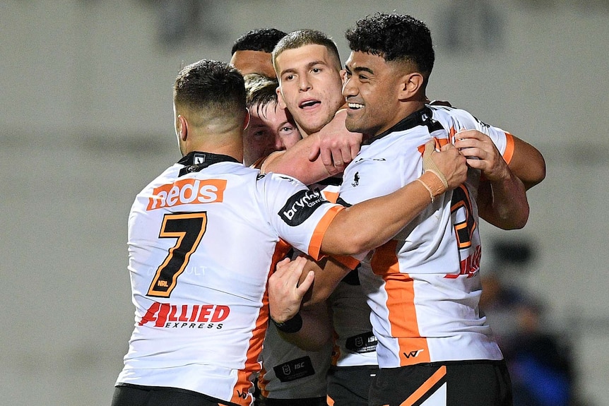 Five Wests Tigers NRL players embrace as they celebrate a try against Manly.