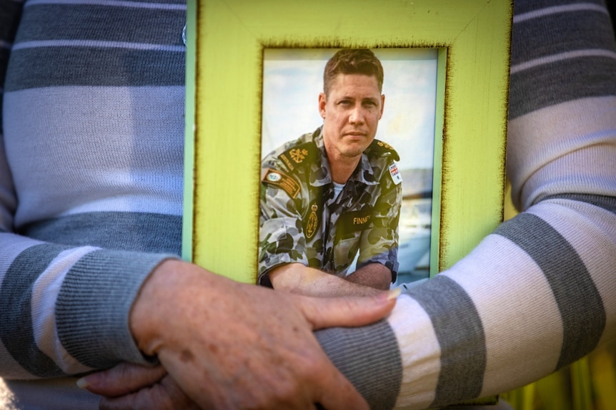 A woman holds a photo of a man in a Navy uniform.