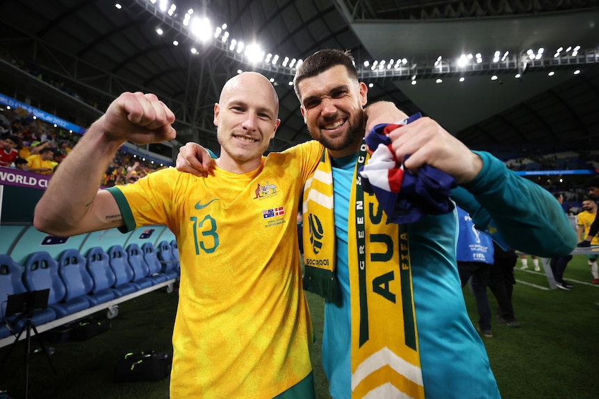 Two Socceroos players pump their fists as they celebrate beating Denmark at the FIFA World Cup.
