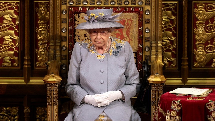 The Queen sits in Parliament wearing a lilac dress and hat