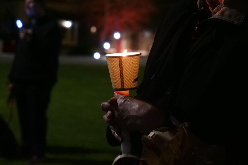 Close up shot of a hand holding a candle at a nightime vigil