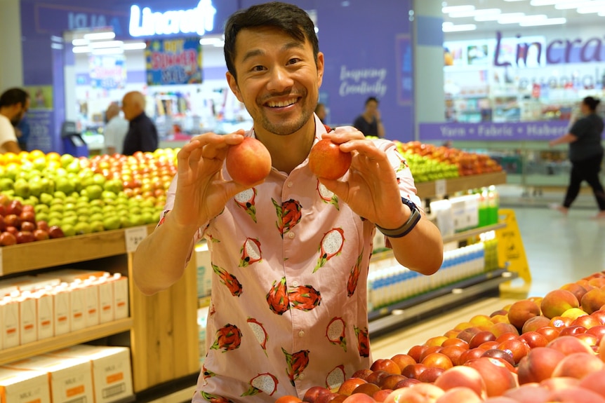 Thanh 'Fruit Nerd' Truong holding two nectarines in a grocery store.