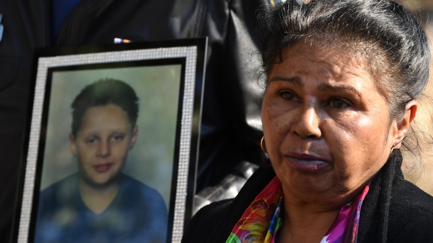 A woman stands next to a photograph of her teenage son who died in a fire.