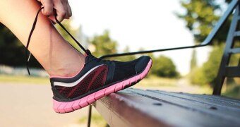 Close-up of a woman tying shoelaces on her running shoes against a park bench.