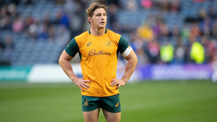 An Australian rugby player stands on the pitch with his hands on his hips.