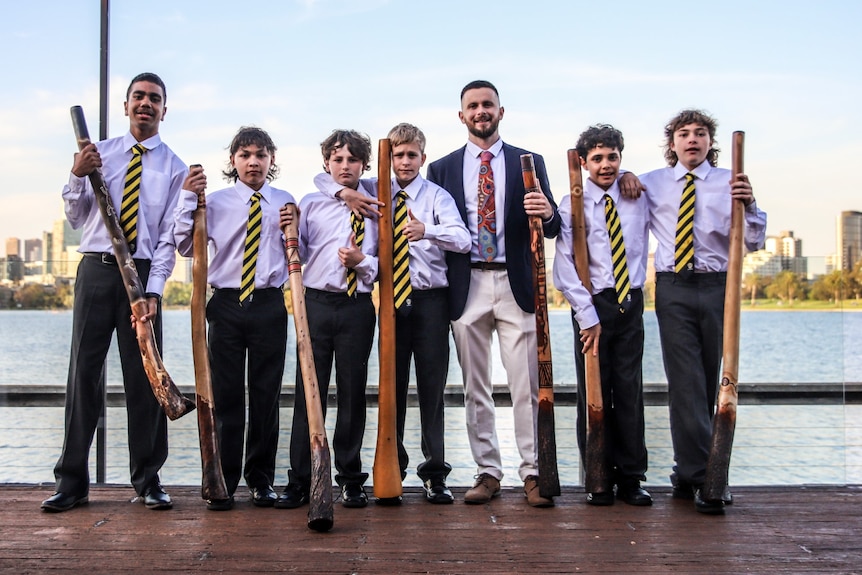 a group of MITS students holding yidakis and wearing shirts and ties standing with teacher Jayden Cooke