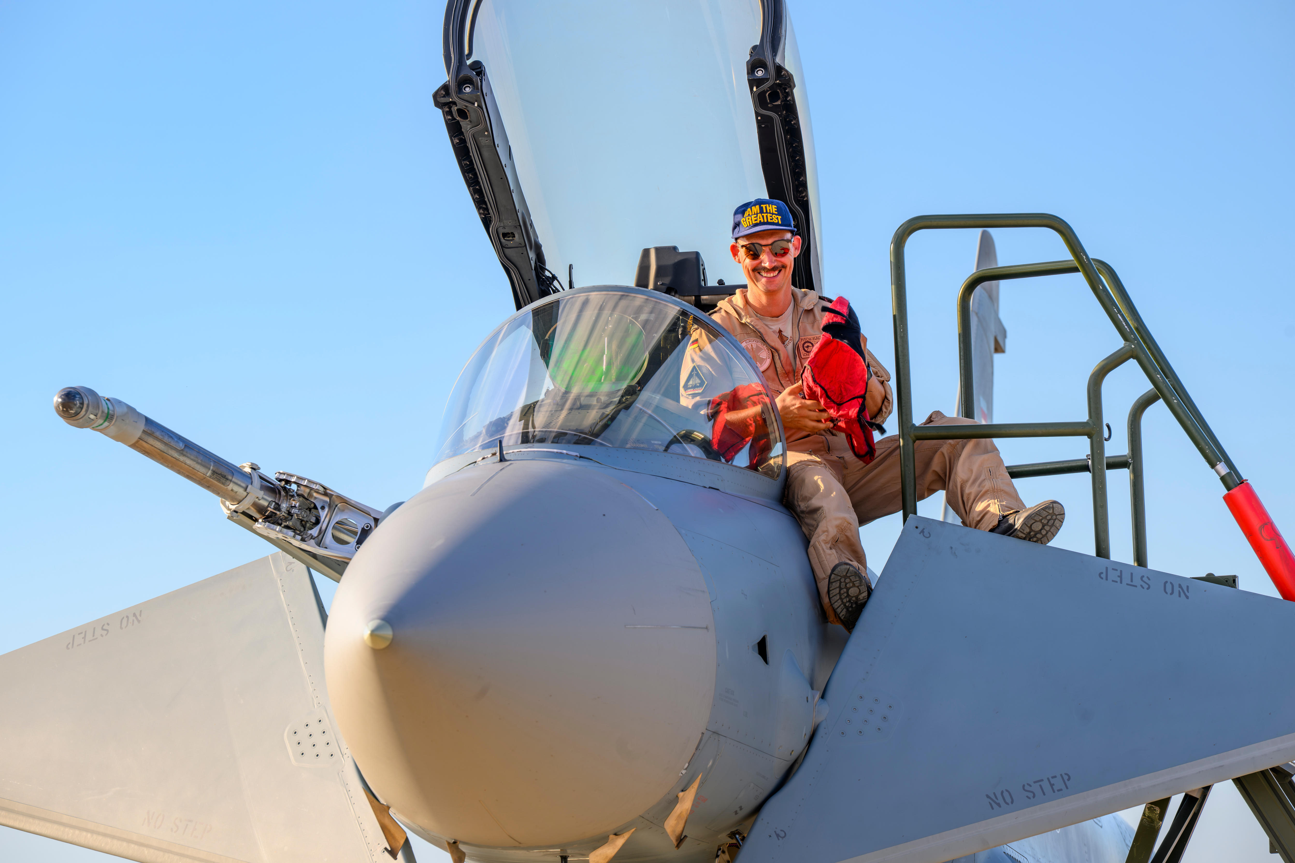 An aviator sits on the edge of a fighter jet's open cockpit.