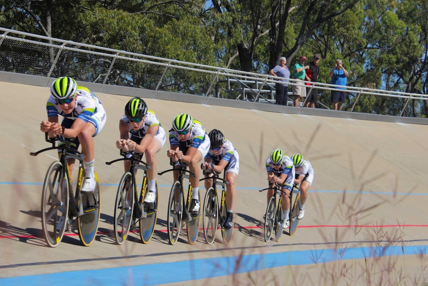 Six cyclists train on a concrete track with a small group of people watching on.