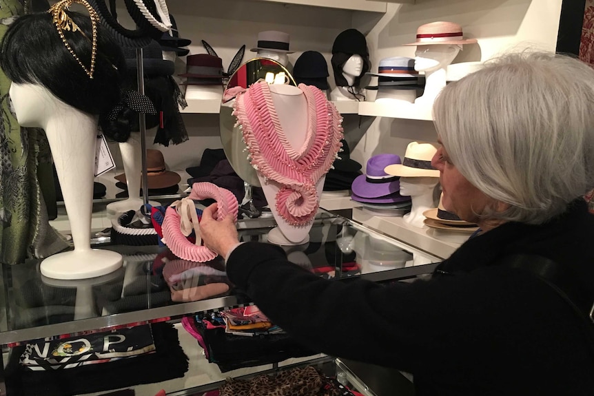 A woman, viewed from behind, places an accessory on display in a boutique store.