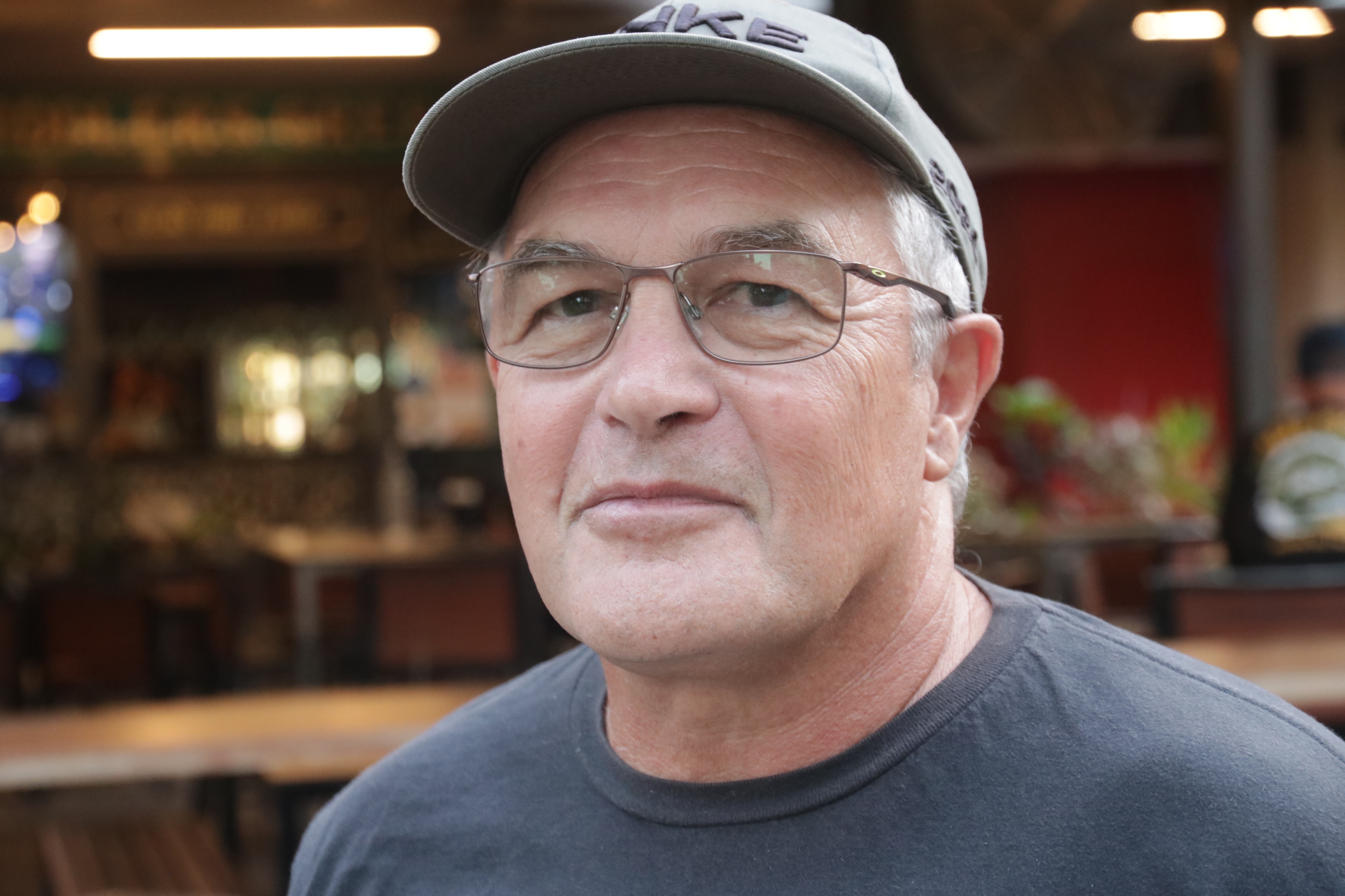 A close up of a man in a grey cap with the shoulders of his black shirt visible