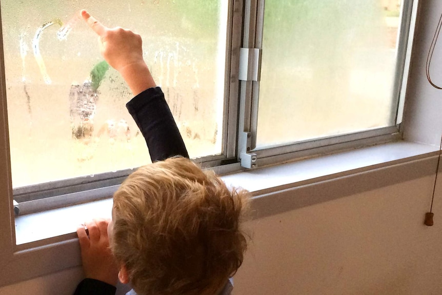 Little boy draws pictures in window condensation