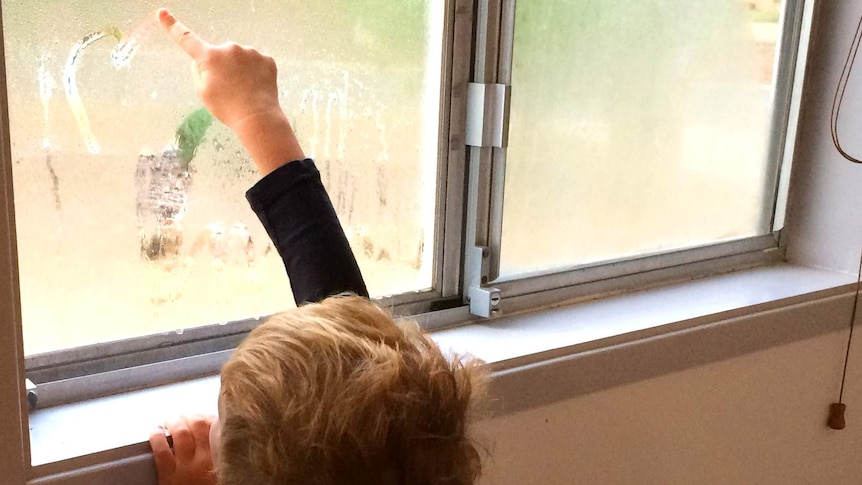 Little boy draws pictures in window condensation