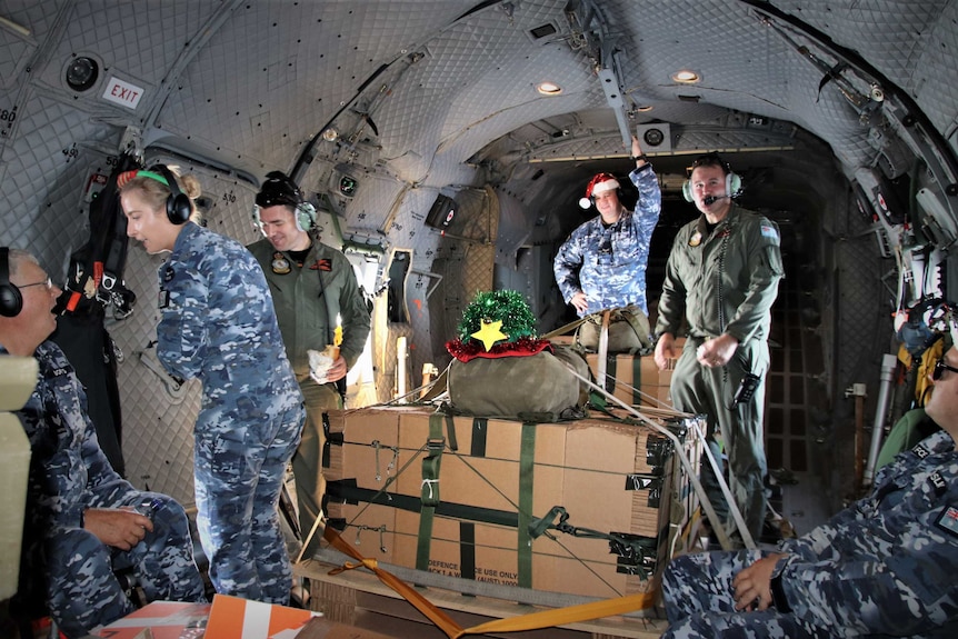 Interior of military plane, Defence personnel including one wearing a Christmas hat and boxes of supplies decorated with tinsel