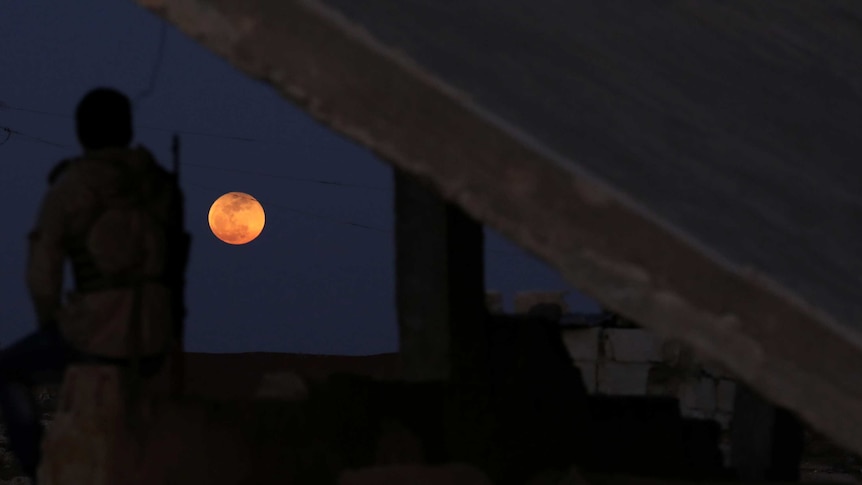 A fighter from Free Syrian Army watches a full moon rises in Daraa