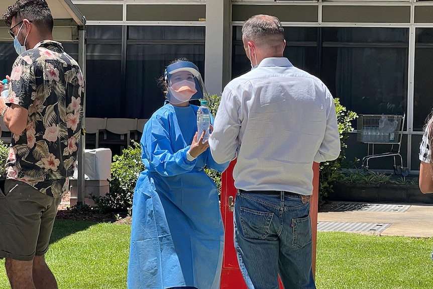 Une femme en tenue de protection distribue des bouteilles d'eau aux personnes qui attendent