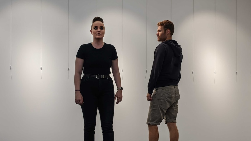 Marie Campbell and Josh Edelyi-Gotz stand on a stage facing opposite directions.