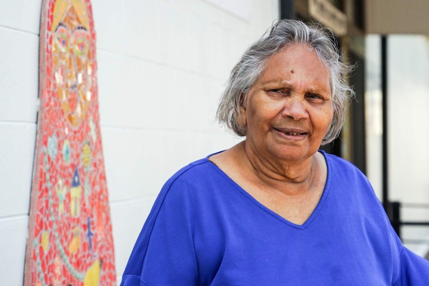 An elderly lady in a bright blue tshirt smiling.