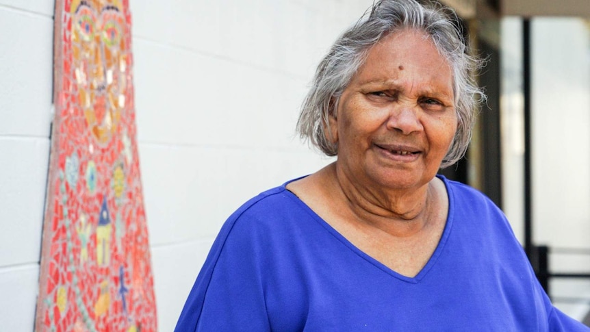 An elderly lady in a bright blue tshirt smiling.