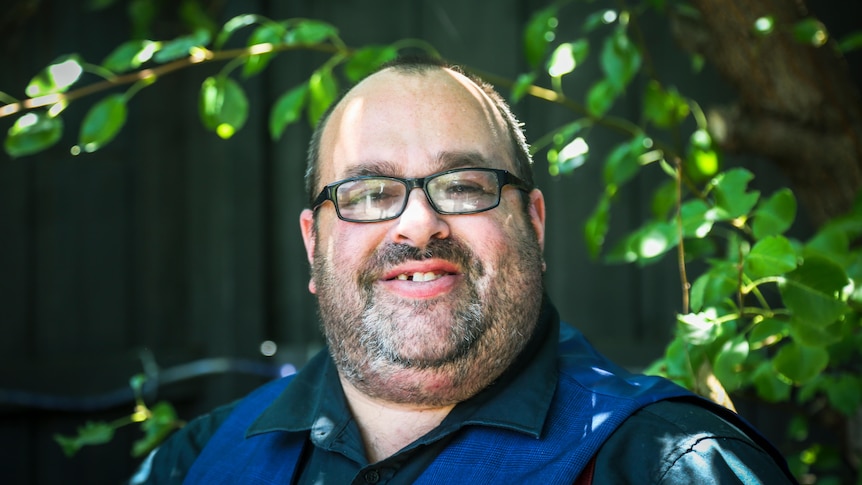 Cameron Bloomfield stands outside in dappled light, smiling at the camera.