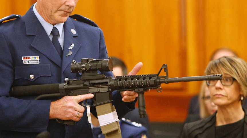 A New Zealand police officer holds an assault rifle in front of parliamentarians.